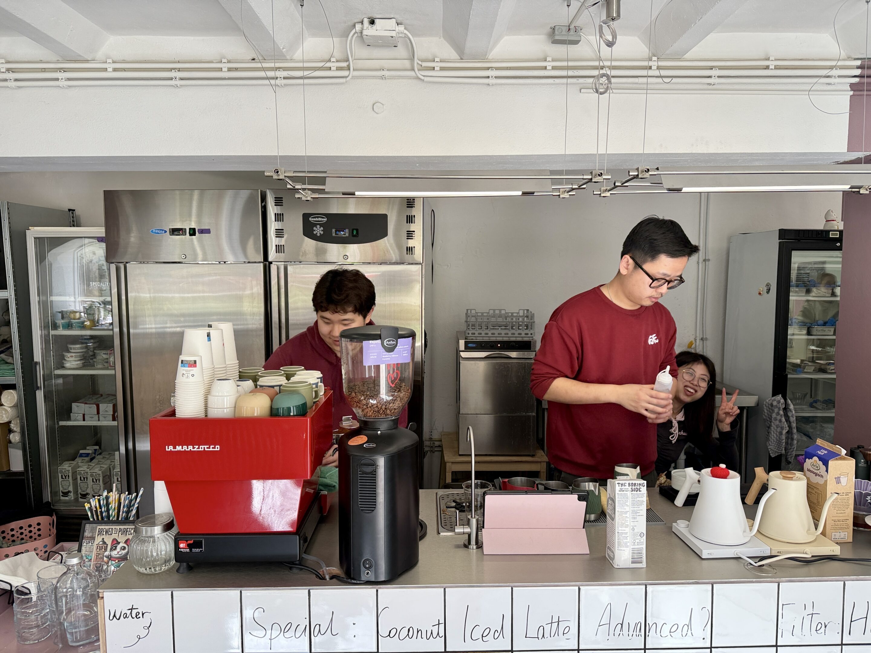 View of a coffee bar with a red espresso machine on the bar and two baristas at work